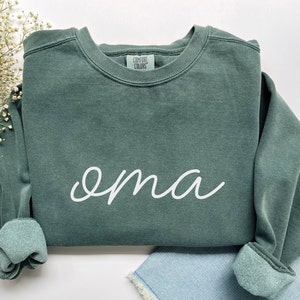 May include: A dark green sweatshirt with the word "oma" written in white cursive script.