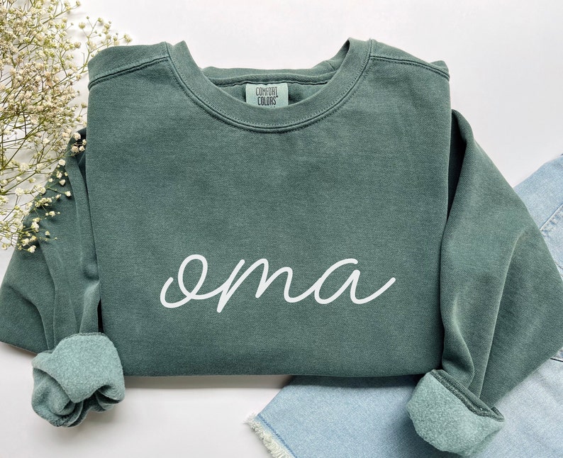 May include: A dark green sweatshirt with the word "oma" written in white cursive script.