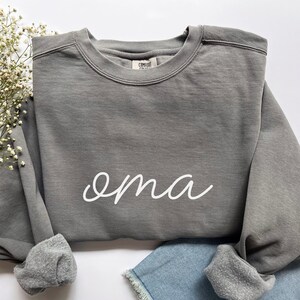 May include: A gray sweatshirt with the word "oma" written in white cursive on the front.