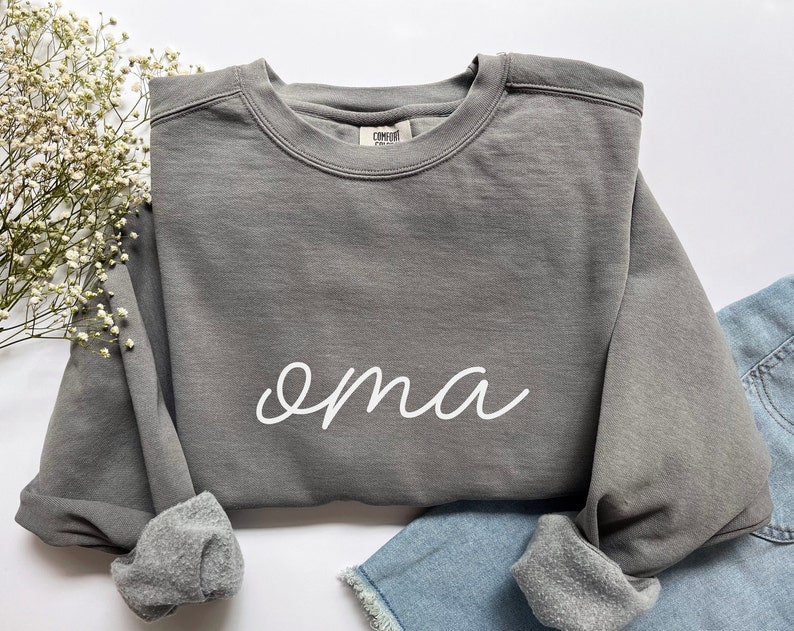 May include: A gray sweatshirt with the word "oma" written in white cursive on the front.