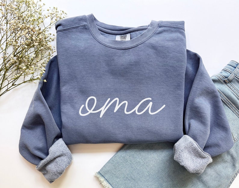 May include: A blue sweatshirt with the word "oma" written in white cursive on the front.