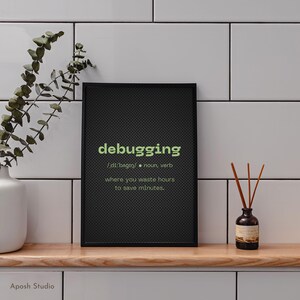 May include: A black framed print with the word "debugging" in green, and its definition. The print is on a wooden surface with a white vase and a small bottle with reeds.