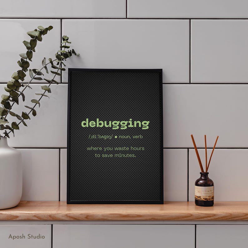 May include: A black framed print with the word "debugging" in green, and its definition. The print is on a wooden surface with a white vase and a small bottle with reeds.
