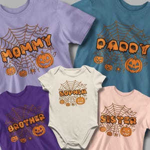 Pode incluir: Uma coleção de camisetas e um body com tema de Halloween em várias cores. Cada camisa apresenta um design de teia de aranha com as palavras "Mommy", "Daddy", "Brother" e "Sister", junto com abóboras. O body diz "Sophia".