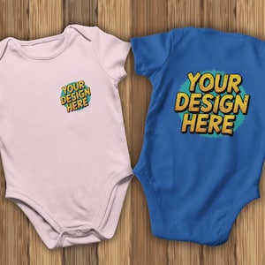 May include: Two baby onesies, one light pink and one blue, are displayed on a wooden surface. The pink onesie has the text "YOUR DESIGN HERE" in a colorful design. The blue onesie has the same text in a similar design.