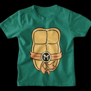 May include: A green t-shirt with a cartoon image of a Teenage Mutant Ninja Turtle's shell. The shell is yellow and orange with a black letter "M" in the center.