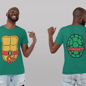 May include: A green t-shirt with a yellow and red turtle shell graphic on the front and a green turtle shell graphic on the back. The turtle shell graphic on the front has a red band with the letter "R" on it.