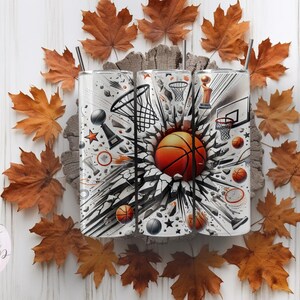 May include: Three stainless steel tumblers with a basketball theme. The tumblers feature a black and white graphic of a basketball breaking through a wall with basketballs, trophies, and a basketball hoop. The tumblers are surrounded by fall leaves.