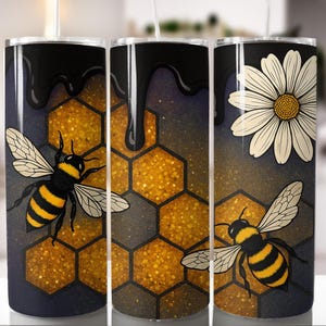 Puede incluir: Tres vasos de acero inoxidable con diseños de abejas y panales. Los vasos presentan una parte superior negra con miel goteando, un patrón de panal y una abeja con rayas amarillas y negras. Un vaso tiene una margarita blanca.