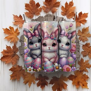 May include: Three stainless steel tumblers with a pastel pink, purple, and blue Easter bunny design. Each bunny is holding an Easter egg and surrounded by flowers.
