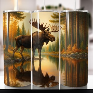 Puede incluir: Un vaso de acero inoxidable con una pintura detallada de un alce de pie en un lago, rodeado de un bosque. La obra de arte muestra colores cálidos de naranja, marrón y amarillo, con el reflejo del alce en el agua. El vaso es para bebidas frías y calientes.