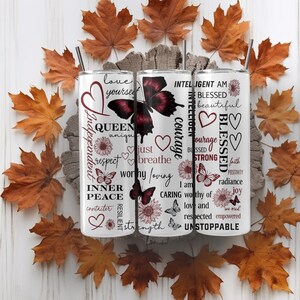 May include: Three white stainless steel tumblers with black straws, decorated with butterflies, hearts, and inspirational words like "Queen", "Blessed", and "Unstoppable". The tumblers are surrounded by autumn leaves.