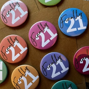 May include: Nine round, colorful buttons with the text "Finally 21" in black script. The buttons are various shades of pink, blue, green, and brown.