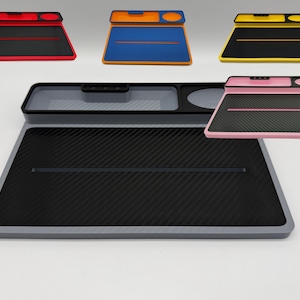 Peut inclure: Une collection d'organisateurs de bureau rectangulaires avec une surface texturée en fibre de carbone, une fente horizontale et une section de rangement supérieure avec un petit compartiment rectangulaire et une empreinte circulaire, en rouge, bleu, jaune, rose et gris.