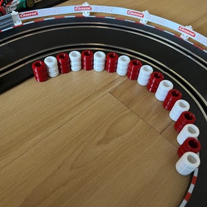 Puede incluir: Una pista de carreras negra con barreras rojas y blancas y barreras de neumáticos rojas y blancas. La pista está configurada en un círculo con un coche en la pista.