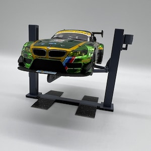 May include: A green and yellow race car is lifted on a gray car lift. The car has a black front spoiler and a black rear wing. The car lift has two gray metal arms and two gray metal bases.