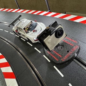 Könnte beinhalten: Ein weiß-schwarzes Rennwagen mit einem Spinnennetz-Design und dem Text "Audi Financing" an der Seite. Das Auto befindet sich auf einer Rennstrecke mit einem schwarz-rot gestreiften Rand. Eine schwarze und silberne Action-Kamera ist auf einem schwarzen Ständer mit dem Text "Camera Slide" montiert.