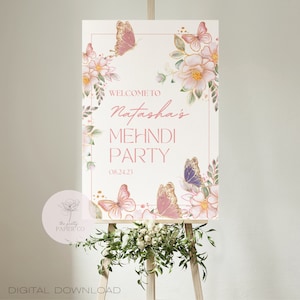 May include: A white sign with pink and gold floral designs and butterflies. The sign says "Welcome to Natasha's Mehndi Party 08.24.23".