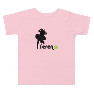 Puede incluir: Camiseta rosa para ni&ntilde;o peque&ntilde;o con una silueta negra de una jugadora de tenis y la palabra "serena" con una pelota de tenis verde.