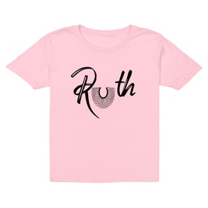 May include: Pink children's t-shirt with a black graphic of the text "Ruth" with a stylized black collar design.