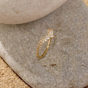 May include: A gold ring with a V-shaped design set with small clear stones.