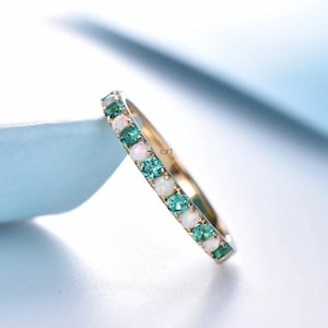 Peut inclure: Une délicate bague en or avec des opales blanches et des pierres précieuses vertes alternées. La bague est sertie de petites pierres rondes.