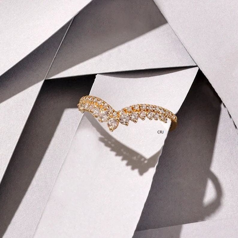 May include: A gold ring with a V-shaped design set with small, clear stones. The ring is on a white background.