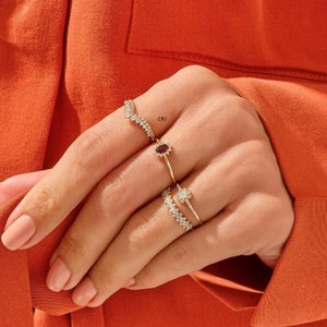 May include: A set of four gold rings with clear and red gemstones. The rings are stacked on a finger. The rings are delicate and sparkly.