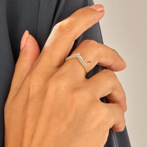 May include: A gold ring with a V-shaped design set with small clear stones. The ring is on a person's finger.