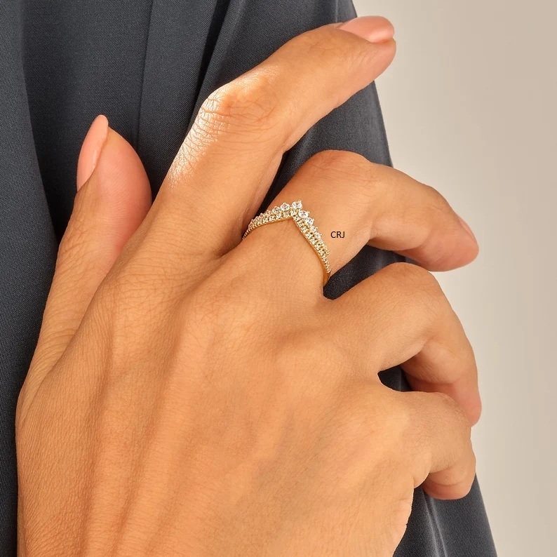 May include: A gold ring with a V-shaped design set with small clear stones. The ring is on a person's finger.