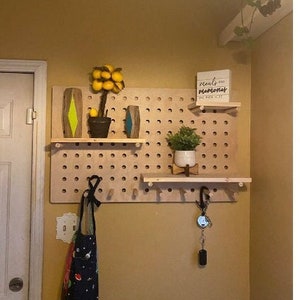May include: A pegboard wall organizer with three shelves, a small potted plant, a lemon tree, and a sign that reads "meals + memories are the best kind".