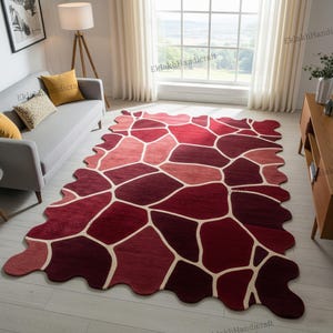 May include: A large, irregularly shaped rug with a pattern of connected, multi-toned red and burgundy shapes, outlined in off-white. The rug is placed on a light-colored wooden floor in a living room setting.