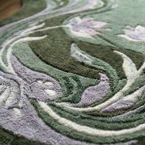 Op de afbeelding: Close-up van een groene vloerkleed met een bloemenontwerp. Het vloerkleed heeft een patroon van wervelende lijnen en gestileerde bloemen in tinten groen, wit en lavendel. De textuur lijkt zacht en pluche.