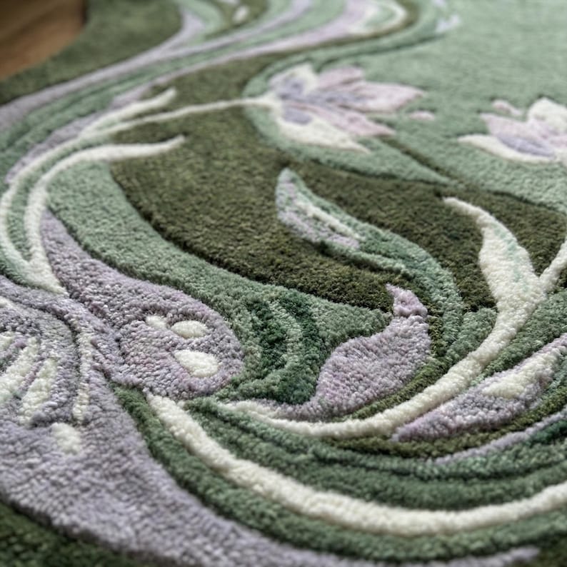 Op de afbeelding: Close-up van een groene vloerkleed met een bloemenontwerp. Het vloerkleed heeft een patroon van wervelende lijnen en gestileerde bloemen in tinten groen, wit en lavendel. De textuur lijkt zacht en pluche.