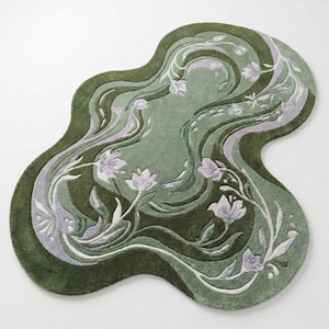 Op de afbeelding: Een decoratief tapijt met een organische vorm, met een bloemenpatroon in groen- en lavendeltinten. Het ontwerp van het tapijt bevat lagen van groene tinten, met witte bloemendetails en stelen. Een decoratief item voor in huis.