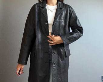 May include: A black leather coat featuring a notched collar, long sleeves, and a front button closure. The coat has a structured fit with vertical seam detailing along the front panels and two side pockets, extending to a mid-thigh length.