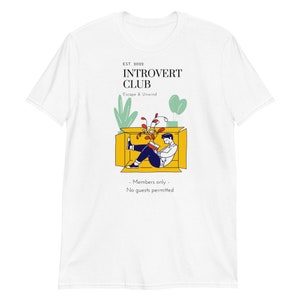 May include: White t-shirt with a graphic of a person sitting in a box reading a book. The text on the shirt reads "EST. 2022 INTROVERT CLUB Escape & Unwind - Members only - No guests permitted"