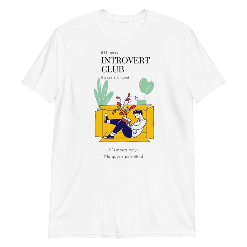 May include: White t-shirt with a graphic of a person sitting in a box reading a book. The text on the shirt reads "EST. 2022 INTROVERT CLUB Escape & Unwind - Members only - No guests permitted"