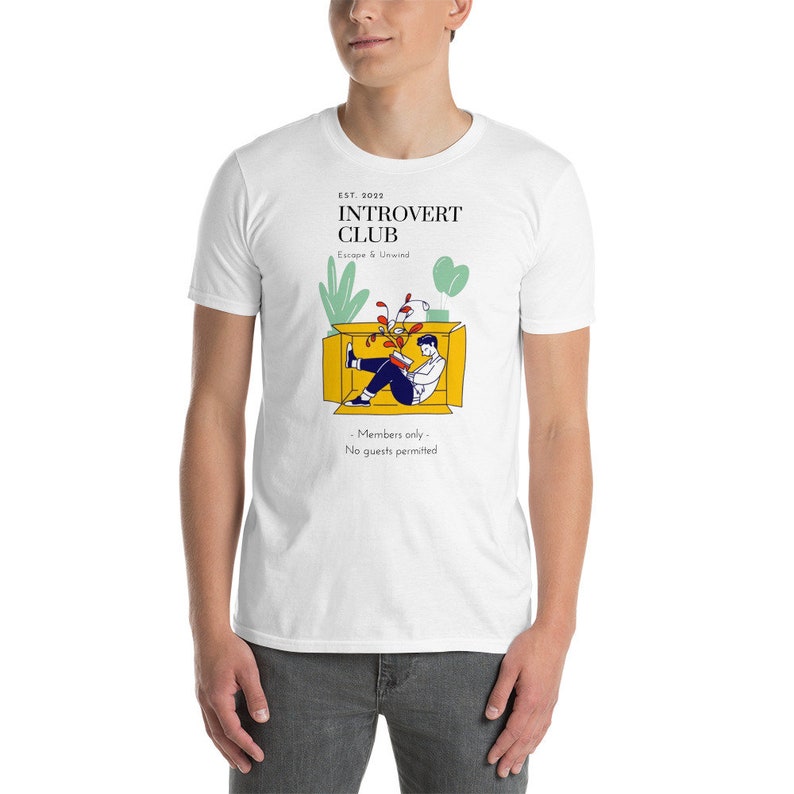 May include: White t-shirt with a graphic design of a person sitting in a box with plants. The text on the shirt reads "EST. 2022 Introvert Club Escape & Unwind - Members only - No guests permitted"