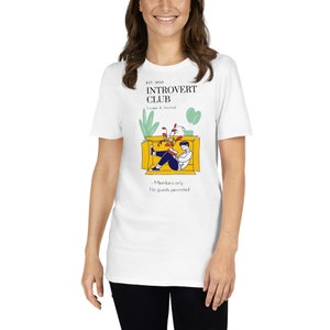 May include: White t-shirt with a yellow box illustration featuring a person reading a book inside. The text on the shirt reads "EST. 9021 INTROVERT CLUB Escape & Unwind - Members only - No guests permitted"