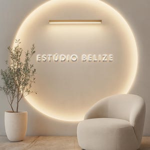 Puede incluir: Un diseño interior moderno con un sillón crema, una planta en maceta y una pared con una luminaria circular. El texto "ESTÚDIO BELIZE" está iluminado en la pared, lo que sugiere un estudio o negocio.