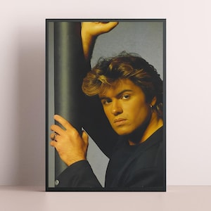 May include: Framed portrait of a man with light brown hair, wearing a black shirt and a gold hoop earring. The man is leaning against a dark, cylindrical object. The portrait is in a black frame.