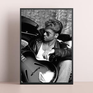 May include: Black and white framed print featuring a man in a leather jacket and sunglasses, holding a guitar. The image has a vintage aesthetic, with the man seated near a motorcycle.