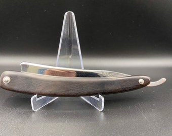 May include: A vintage straight razor with a dark wood handle and a silver blade. The blade is inscribed with the text "DE MARCO" and "MADE IN ITALY".