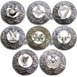 Op de afbeelding: Collectie ronde broches in antieke stijl met diverse emblemen. Ontwerpen omvatten een wereldbol met anker, een vrijmetselaarssymbool, een harp, een hert, een distel, een draak en een kruis. Elke broche is omcirkeld door een bloemmotief.