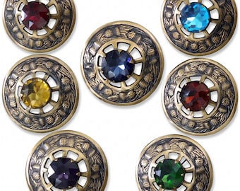 May include: A collection of seven circular metal buttons featuring an antique brass finish with an embossed thistle pattern. Each button has a central faceted gemstone in various colors including red, blue, yellow, dark blue, purple, and green.