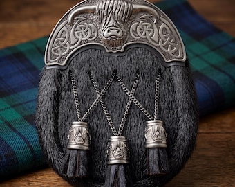 May include: A black fur sporran featuring a silver-toned metal cantle embossed with a Highland cow head and intricate Celtic knotwork. Three matching silver-toned metal tassels with Highland cow engravings hang from thin silver chains.