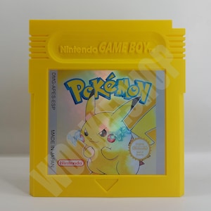 Può includere: Cartuccia gialla Nintendo Game Boy con il gioco Pokémon. La cartuccia presenta il logo Pokémon e un'illustrazione di Pikachu. Il testo "Nintendo GAME BOY" è in alto e "MADE IN JAPAN" è stampato sul lato.