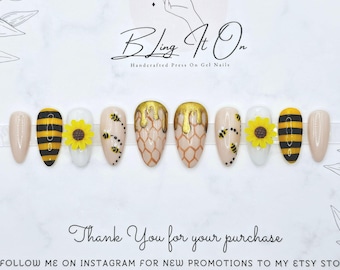 May include: A set of handcrafted press-on gel nails with a bee and sunflower theme. The nails feature designs with gold, black, and yellow accents. The card reads "Bling It On" and "Thank You for your purchase."