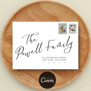 May include: A white envelope with the words "The Powell Family" in elegant script. The address is printed below, with two vintage stamps in the upper right corner. The envelope is on a wooden tray.